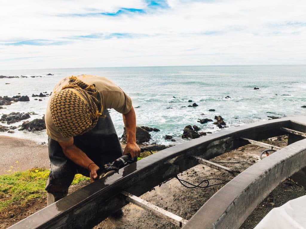 Worker grinding metal frame near ocean shore